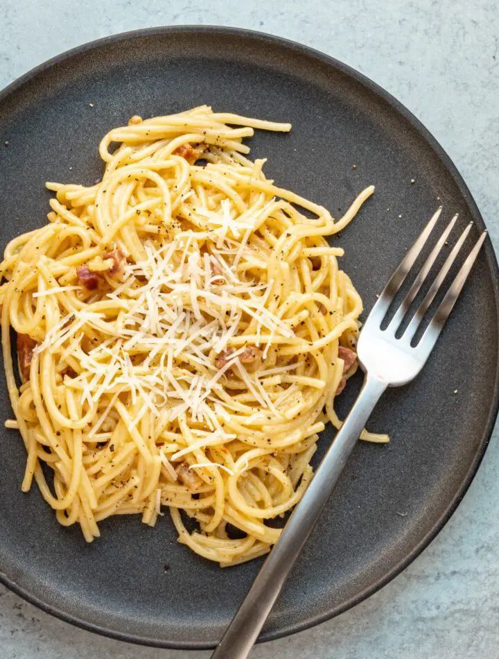 spaghetti carbonara on a plate with fork and parmesan cheese topping