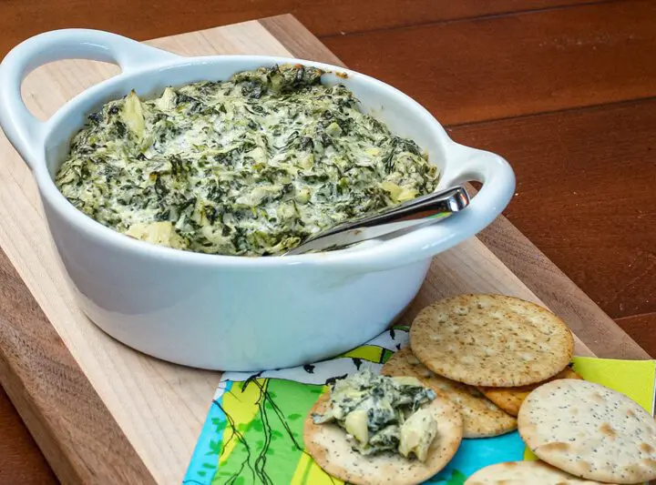 spinach artichoke dip in a baking dish with crackers on the side