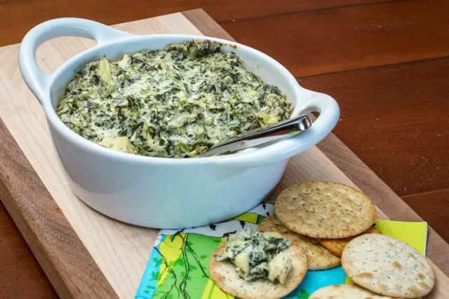 spinach artichoke dip in a baking dish with crackers on the side