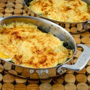 spinach casserole with hard-boiled eggs and cheese sauce in stainless steel gratin dishes