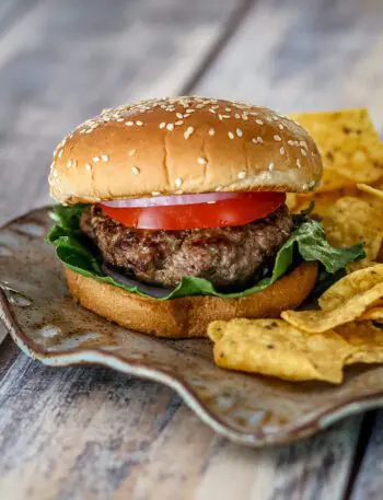 bacon and cheese stuffed burgers on a plate with chips on the side