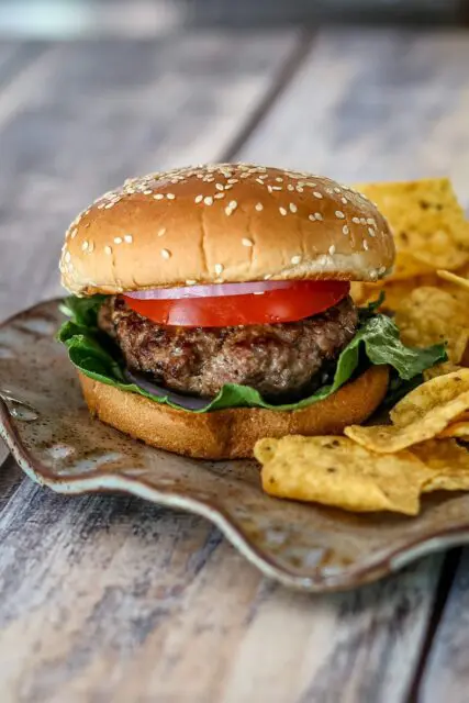 bacon and cheese stuffed burgers on a plate with chips on the side