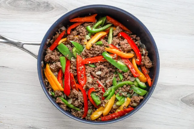 Sautéing peppers and ground beef for a stuffed pepper casserole, an easy one-pot meal made in a skillet.