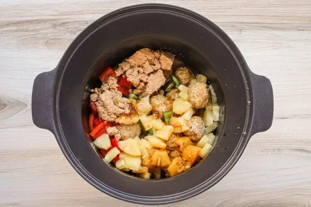 Sweet and sour meatball preparation in the slow cooker, with pineapple, bell peppers, and brown sugar.