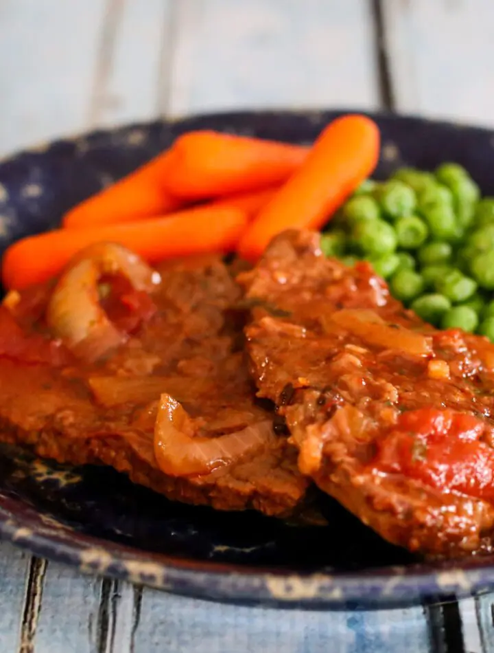 swiss steak on a plate with carrots and peas