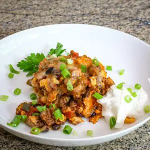 tamale and ground beef ranch casserole on a plate with sour cream on the side