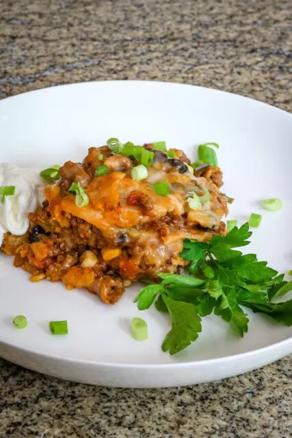 layered tamale casserole with ground beef on a plate with herbs, sour cream, and green onions