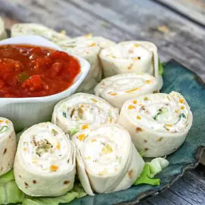 tortilla pinwheel roll-ups on a plate with a small bowl of salsa in the center