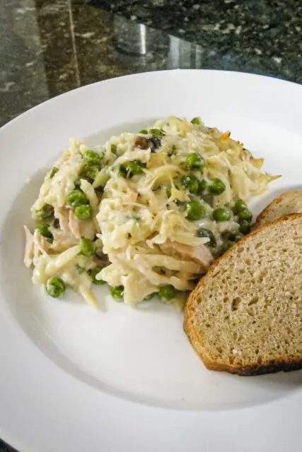 tuna casserole with orzo, peas, and cheese on a plate with sliced bread