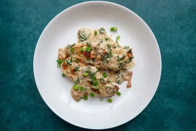 tuscan chicken with sun dried tomatoes, spinach, and a garnish of green onions.