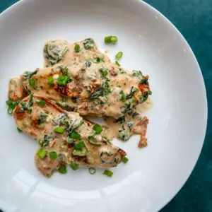 a plate of tuscan chicken with sun dried tomatoes, spinach, parmesan cheese, and creamy sauce