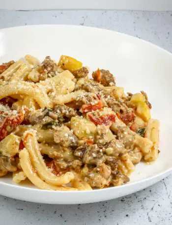 tuscan pasta in a bowl with italian sausage, sun dried tomatoes, and zucchini