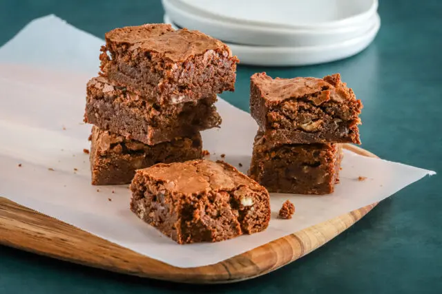 A teak board and parchment paper topped with delicious baked ultimate fudgy brownies.