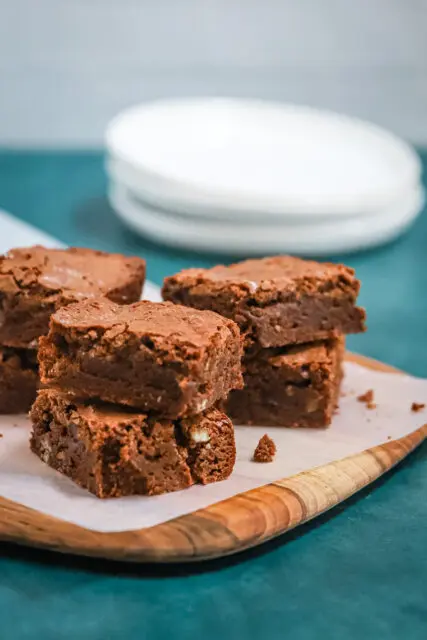 Ultimate fudgy brownies on a parchment paper and teak board, ready to enjoy.