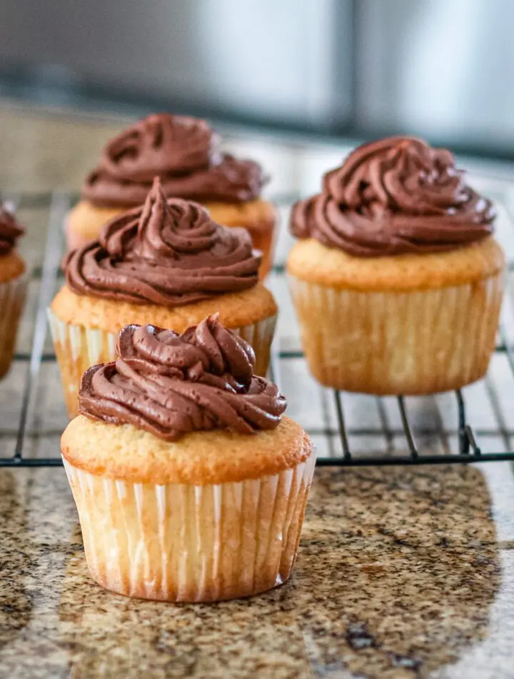 moist vanilla cupcakes on a rack with chocolate frosting