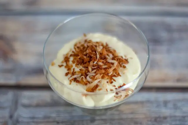 homemade vanilla pudding in a glass dessert dish with toasted coconut