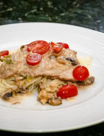 veal marsala with cream sauce on a plate with angel hair pasta.