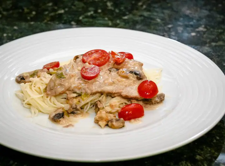 veal marsala with cream sauce on a plate with angel hair pasta.