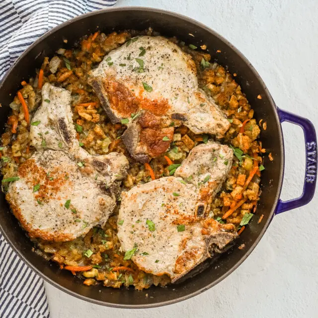 A large Staub sauté pan with seasoned stuffing and pork chops baked in the oven.