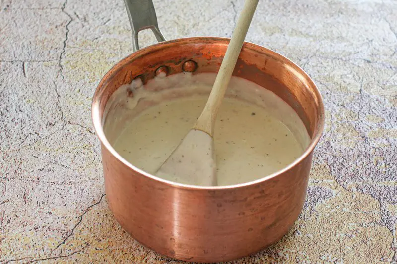 basic white sauce in a copper saucepan with wooden spoon
