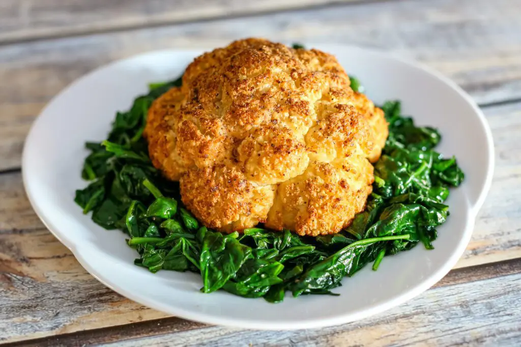 a whole roasted head of cauliflower on a platter with steamed spinach