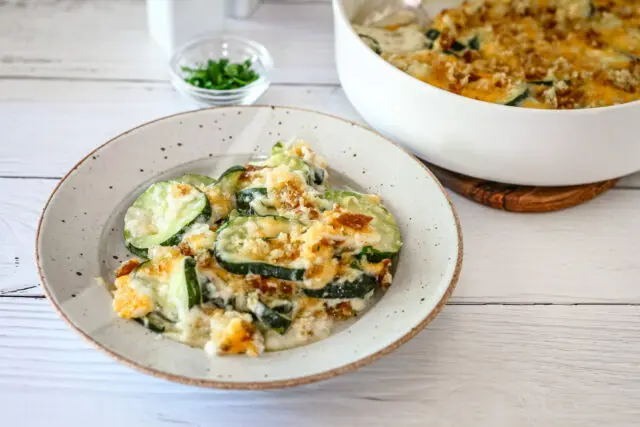 Zucchini casserole on a plate with the baking dish in the background.