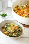 Zucchini casserole on a plate with the baking dish in the background.