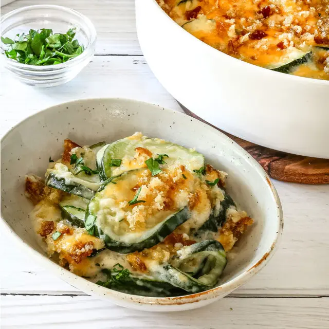 Zucchini casserole on a plate with the baking dish in the background.