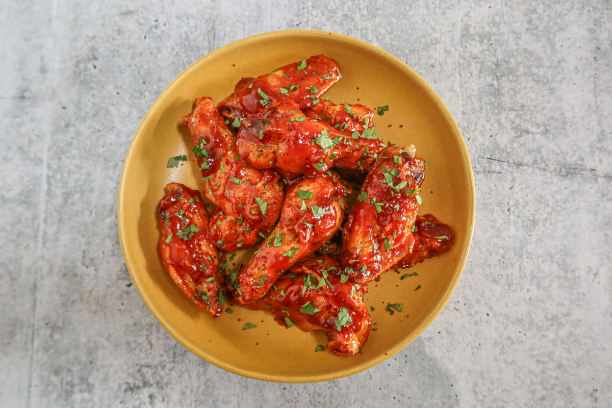 A serving bowl with air fryer Korean chicken wings in spicy sauce with cilantro and gochugaru garnish.
