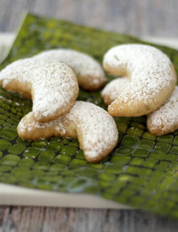 almond crescent cookies on a plate with powdered sugar dusting