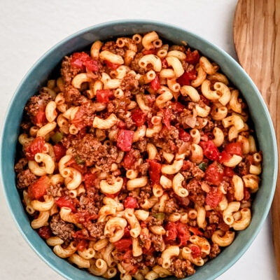 A serving bowl of American chop suey with a wooden spoon beside it.