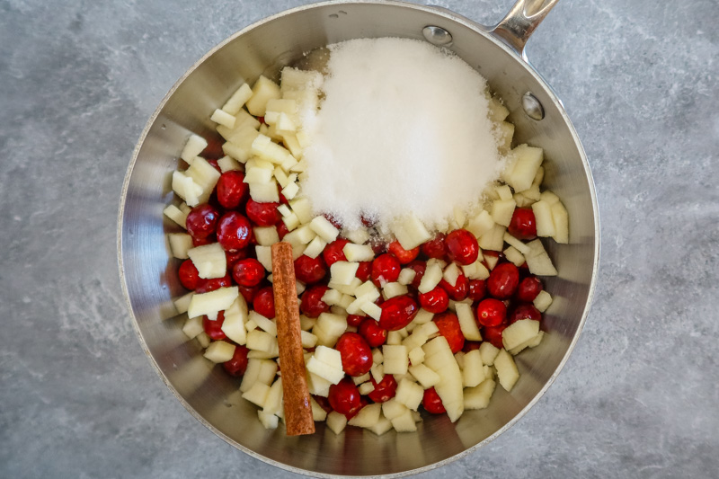 cranberry sauce prep in a saucepan with diced apples, cranberries, sugar, and cinnamon stick.
