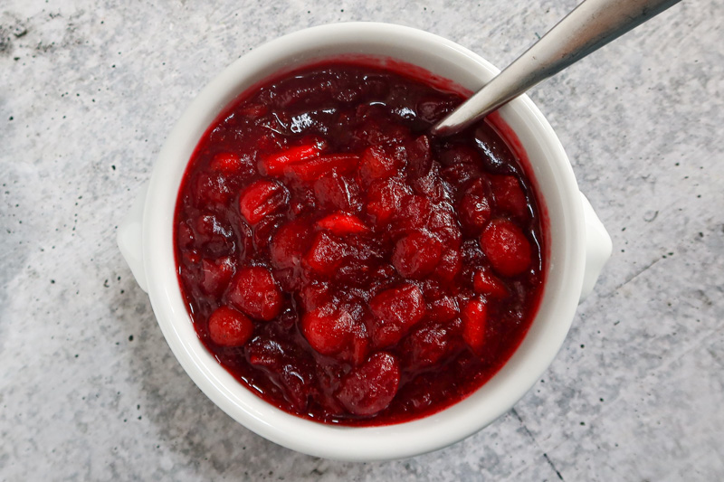 A bowl of apple cider cranberry sauce with a serving spoon.