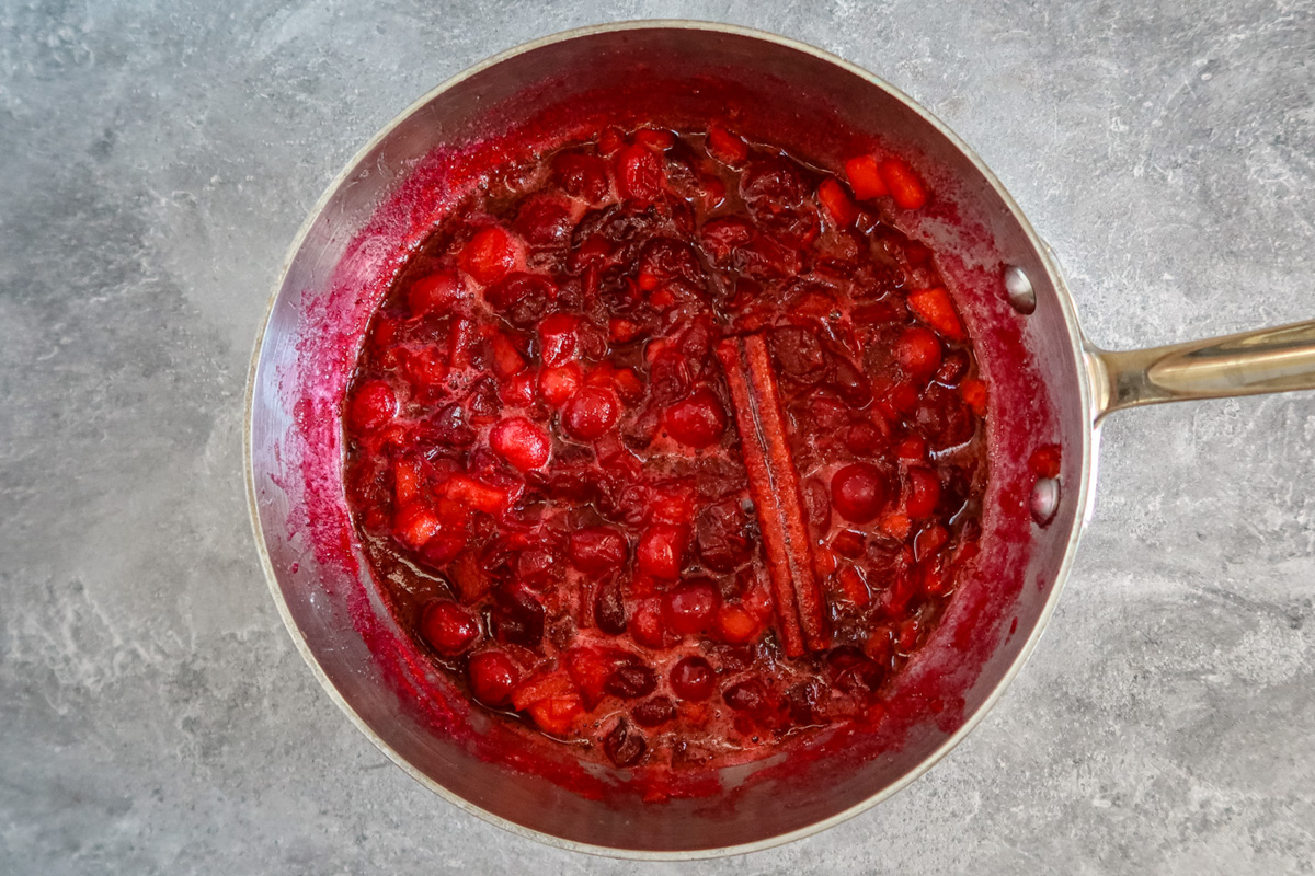 cranberry sauce prep in a saucepan with diced apples, cranberries, sugar, and cinnamon stick.