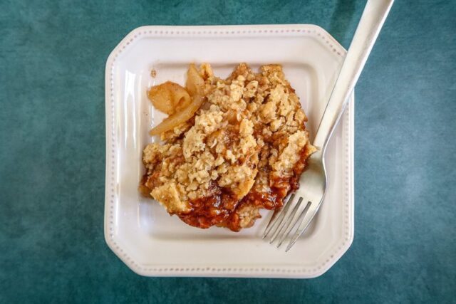 baked homemade apple crisp on a plate with a fork on the side.