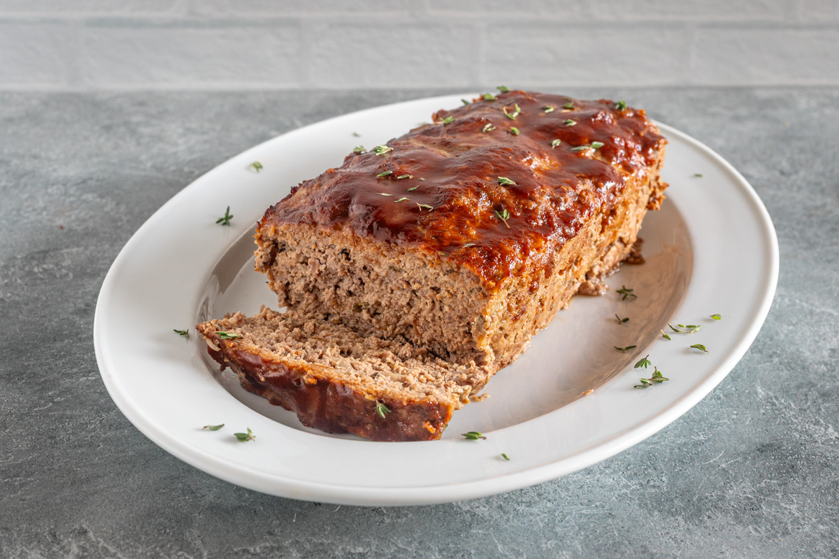 bbq meatloaf on a white platter with thyme leaves scattered around it.