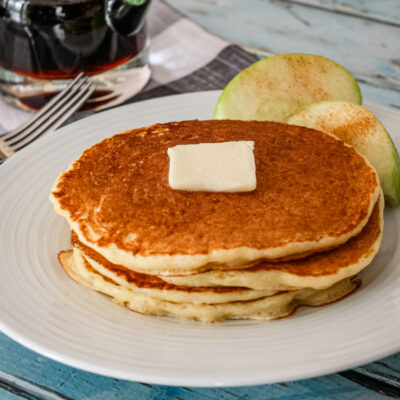 Cornmeal pancakes on a white plate with syrup in the background.