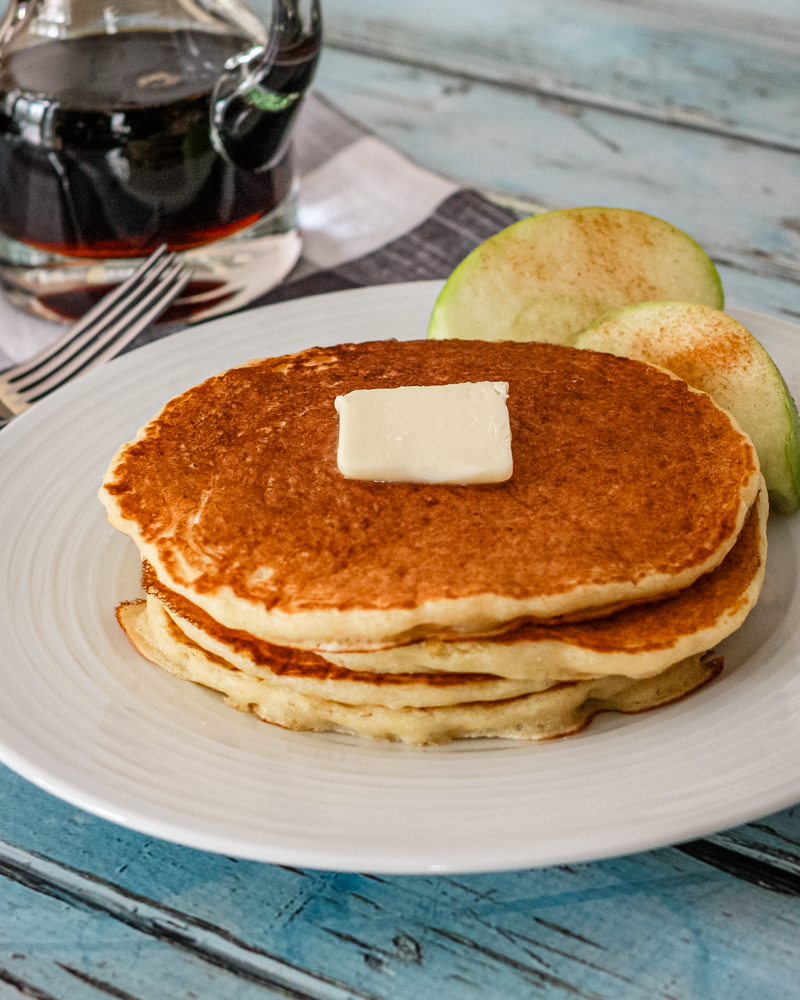 Cornmeal pancakes on a white plate with syrup in the background.