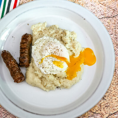 Cheese grits shown with a poached egg and sausages.