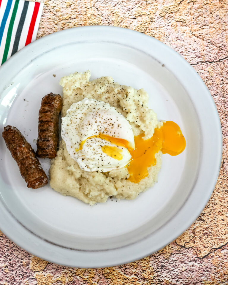 Cheese grits shown with a poached egg and sausages.