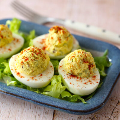 Deviled eggs garnished with paprika on a blue plate.