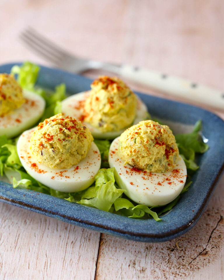 Deviled eggs garnished with paprika on a blue plate.