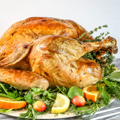 A whole roasted turkey on a platter surrounded by fruit and herbs.