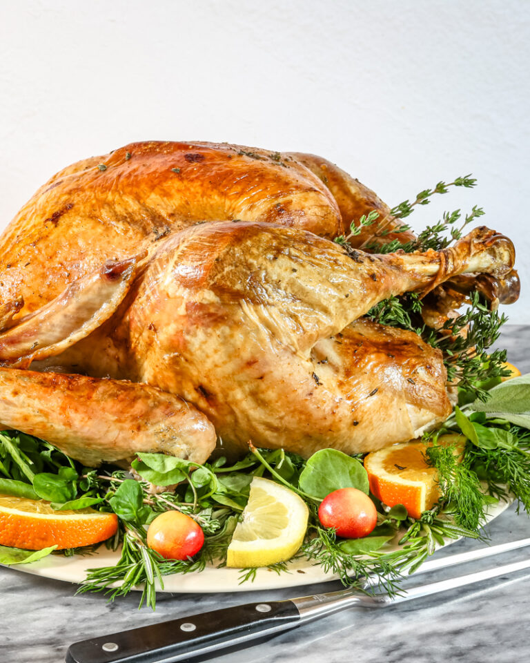A whole roasted turkey on a platter surrounded by fruit and herbs.
