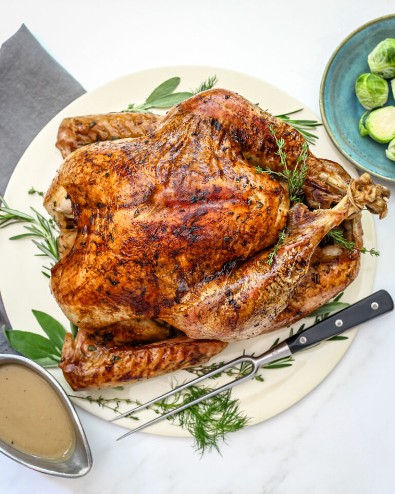 A whole roasted turkey with herbs surrounding it, and a dish of brussels sprouts on the side.