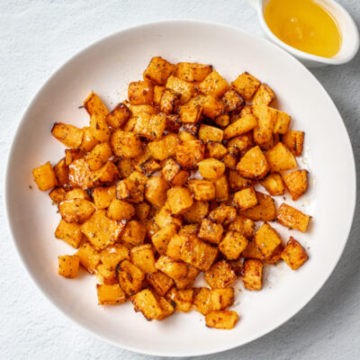 A platter of glazed roasted butternut squash with a small jug of melted butter.
