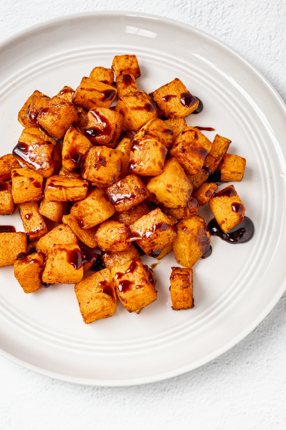 A plate with butternut squash, roasted and drizzled with a balsamic reduction glaze.
