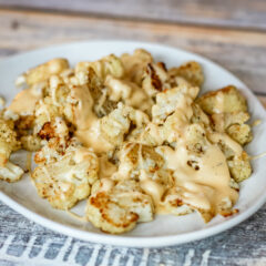 A serving plate with roasted cauliflower, topped with cheese sauce.