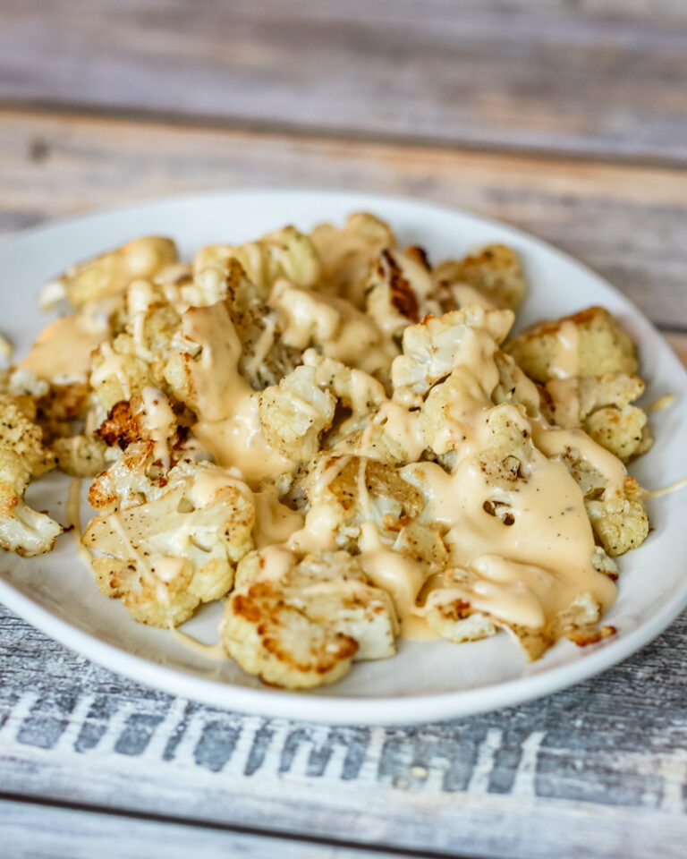 A serving plate with roasted cauliflower, topped with cheese sauce.