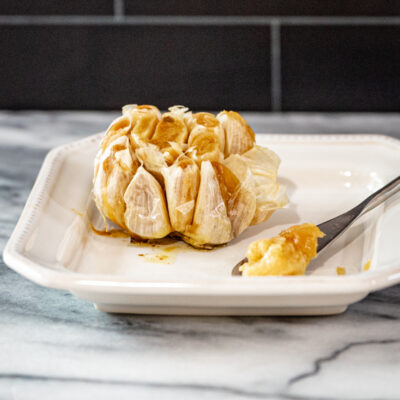 Roasted garlic, a whole head, on a plate with a little spreader.